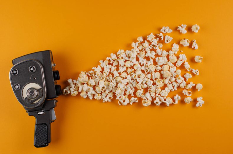 Retro movie camera with popcorn flying out of it on a yellow background. Cinema concept.